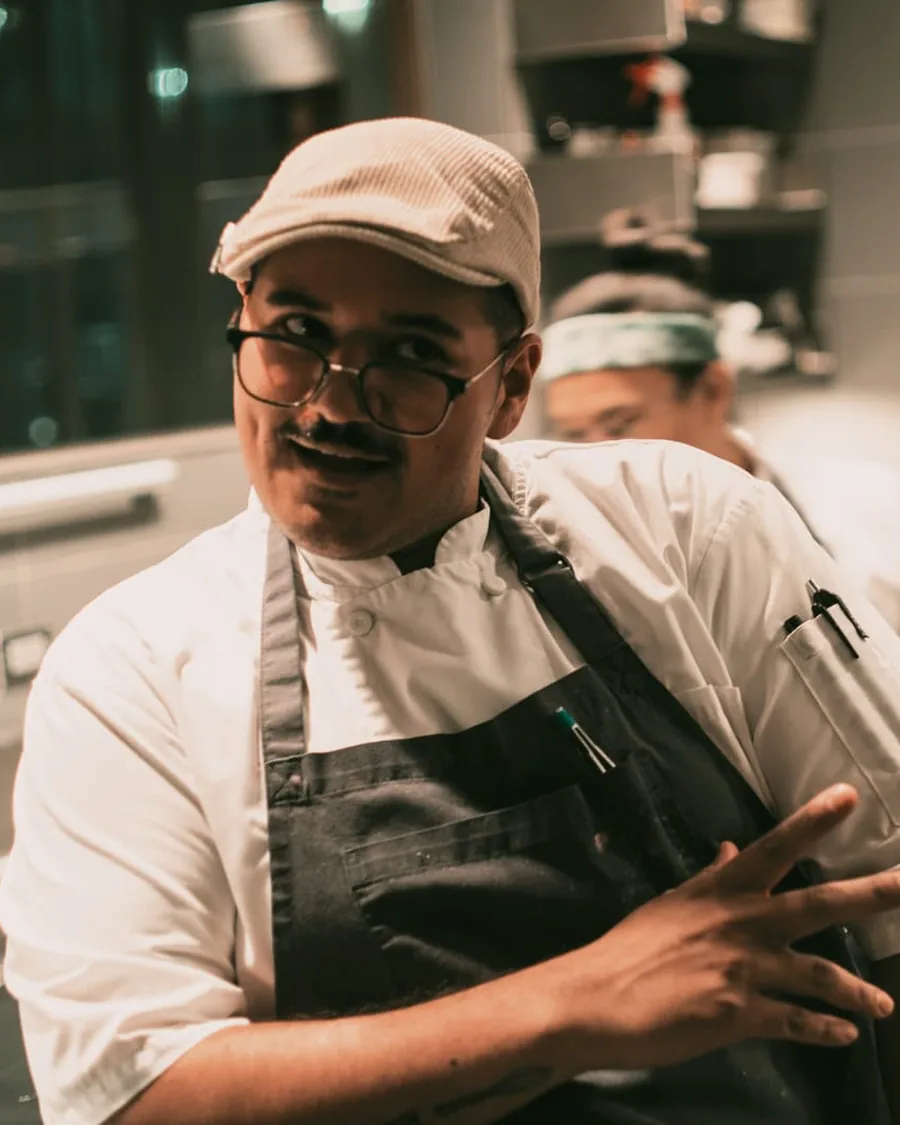 Chef Antonio Coriano smiling in the kitchen, wearing a flat cap and apron